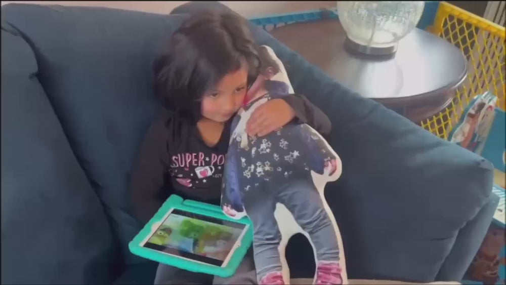Child hugging a personalized funny pillow while playing with a tablet on a couch.